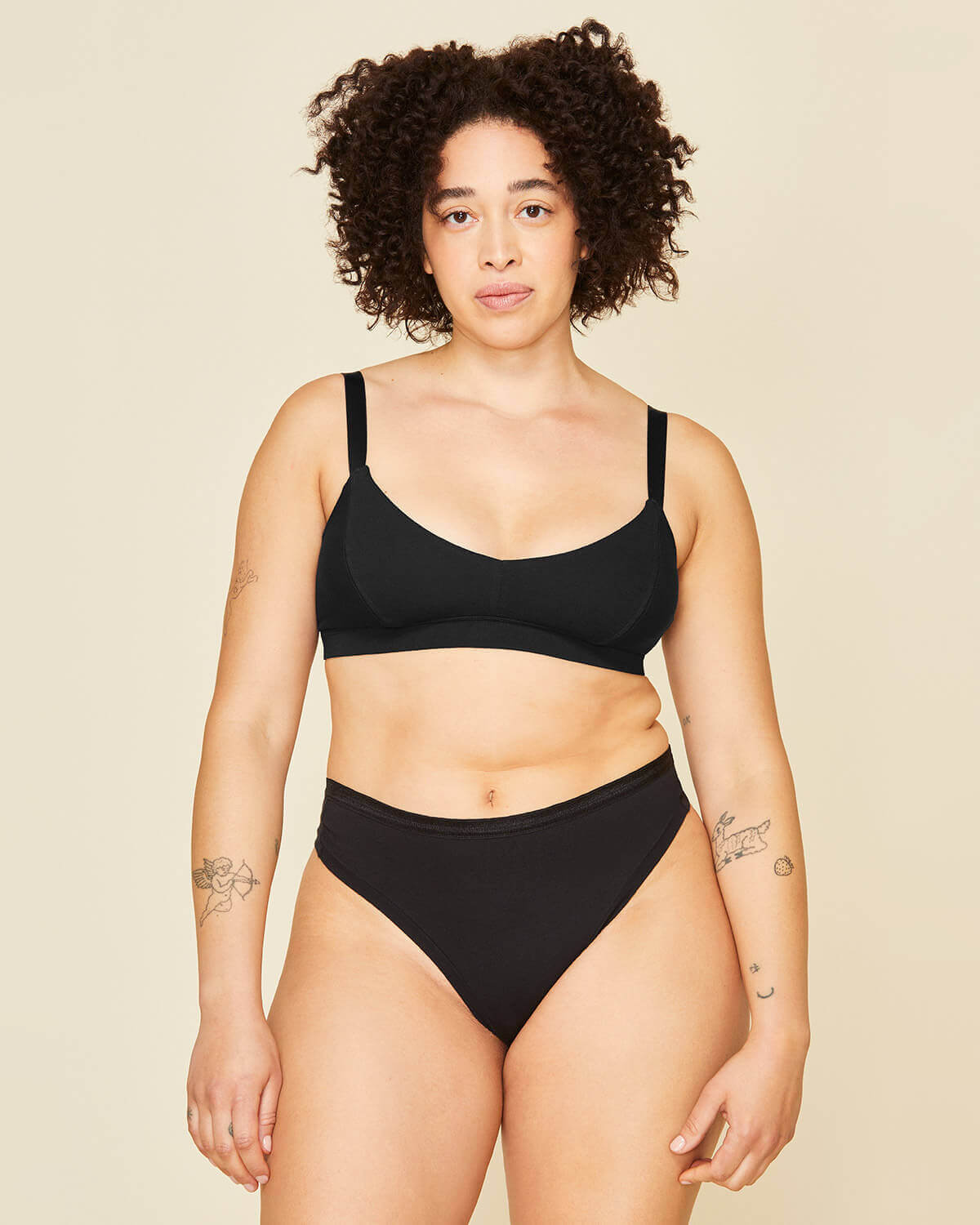 Woman wearing the triangle soft bra in carbon black and the mid rise thong in carbon black color.