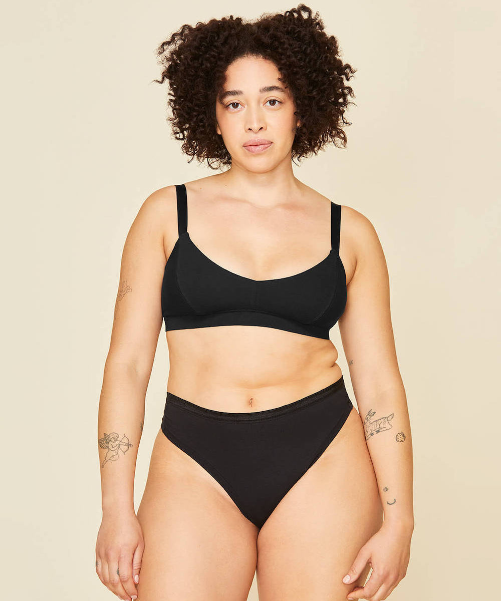 Woman wearing the mid rise thong in carbon black and the triangle soft bra in carbon black color.