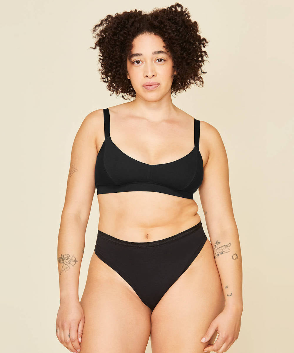 Woman wearing the mid rise thong in carbon black and the triangle soft bra in carbon black color.