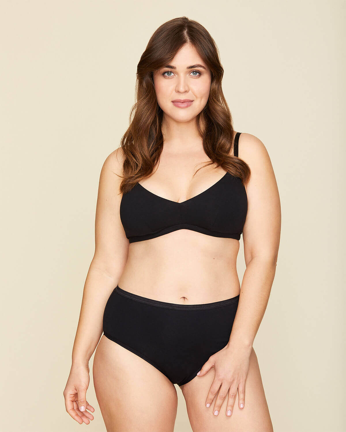 Woman wearing the triangle bra in carbon black and the mid rise briefs in carbon black color.