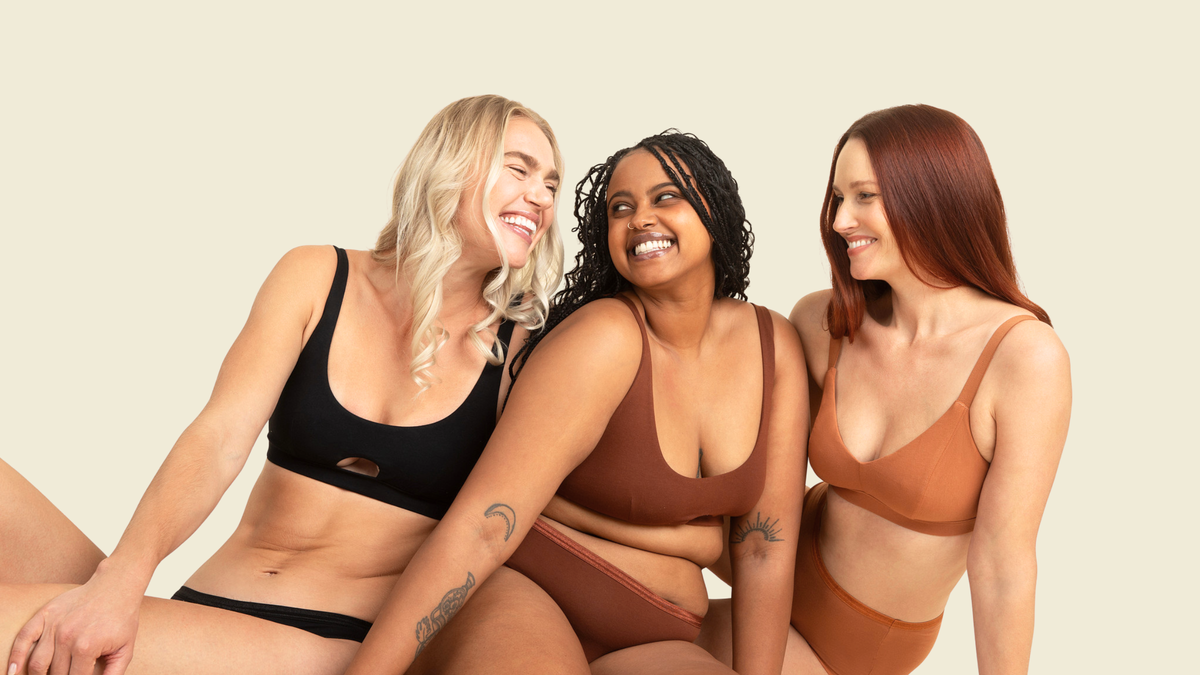 Three women wearing brown and black lingerie sitting together on a beige background
