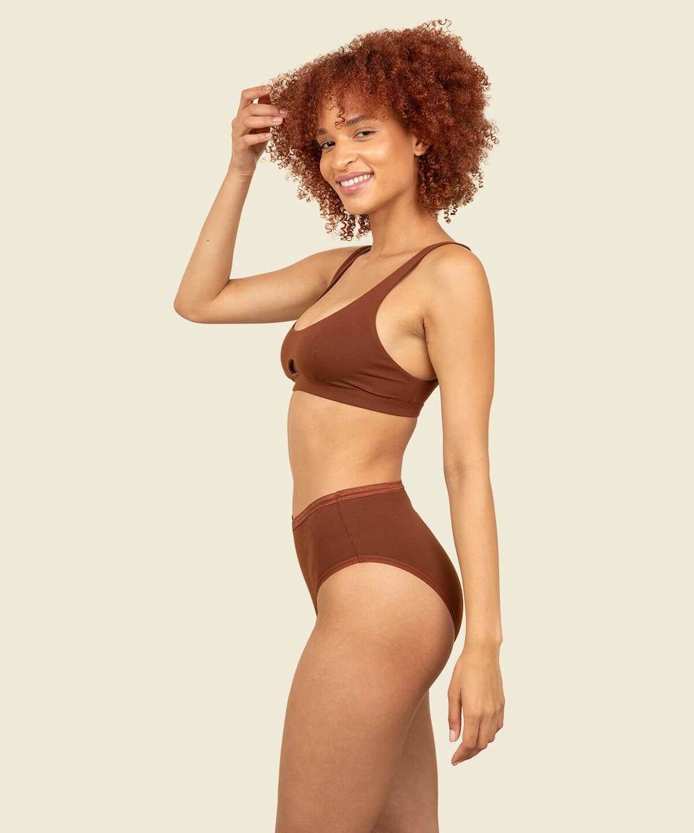 A side view of a woman wearing organic cotton high-rise brief and keyhole soft bra in cacao brown color.
