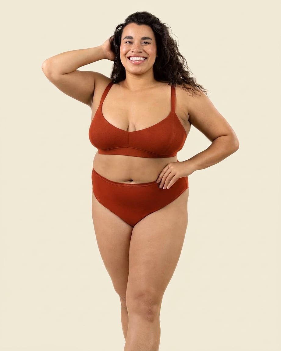 A woman modeling a terracotta-colored high rise brief against a solid light beige background.