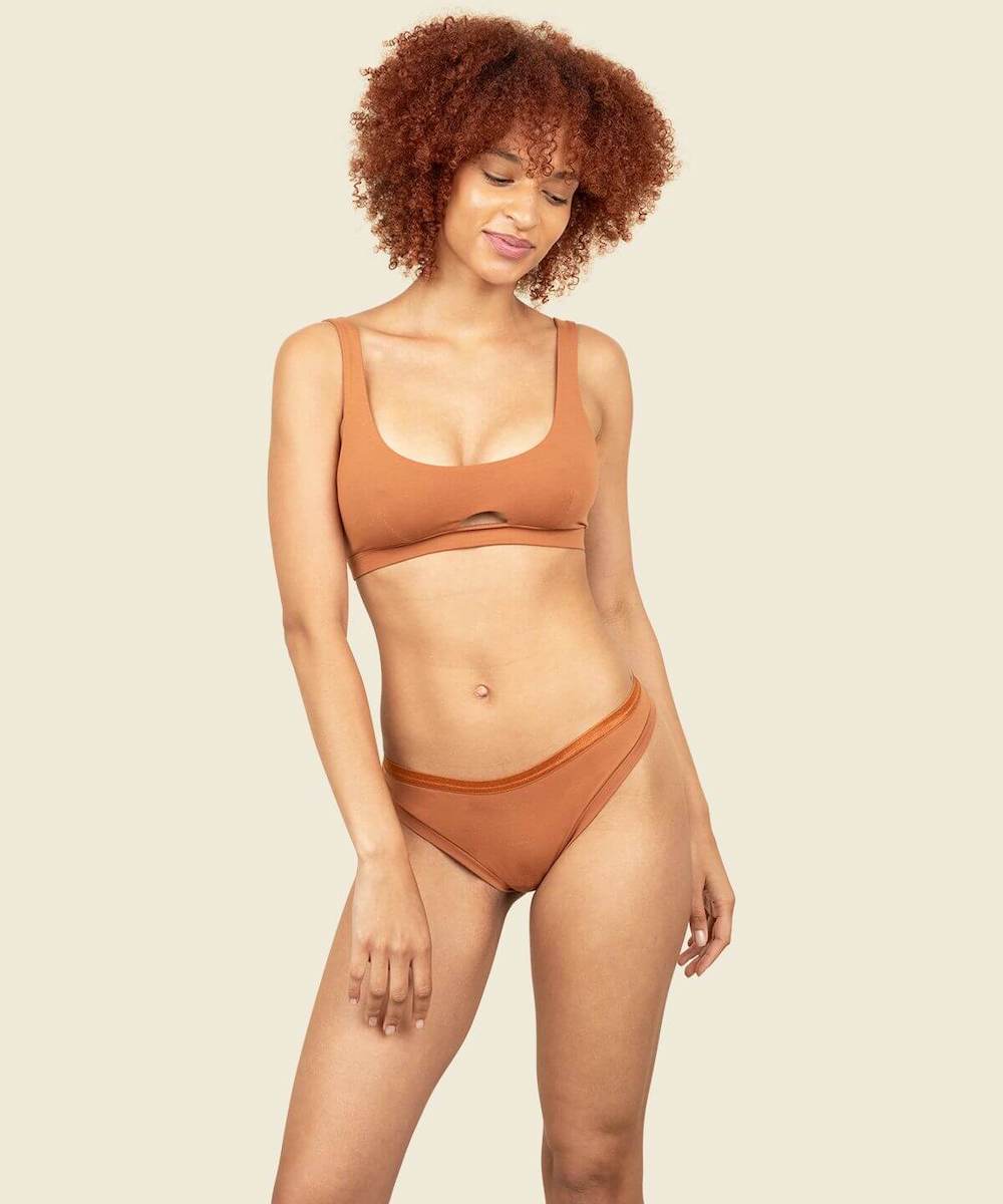 Woman in organic cotton low-rise thong and keyhole soft bra in spice orange brown color.