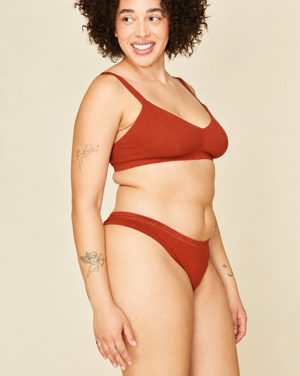 A woman modeling a terracotta-colored low rise thong against a solid light beige background.
