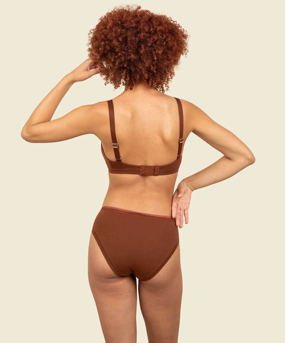 A rear view of a woman wearing organic cotton mid-rise bikini and triangle soft bra in cacao brown color.