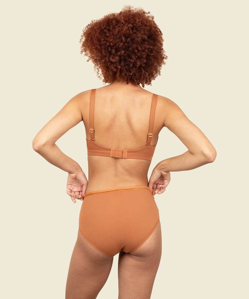 Woman in organic cotton mid-rise brief and triangle soft bra in spice orange brown color.