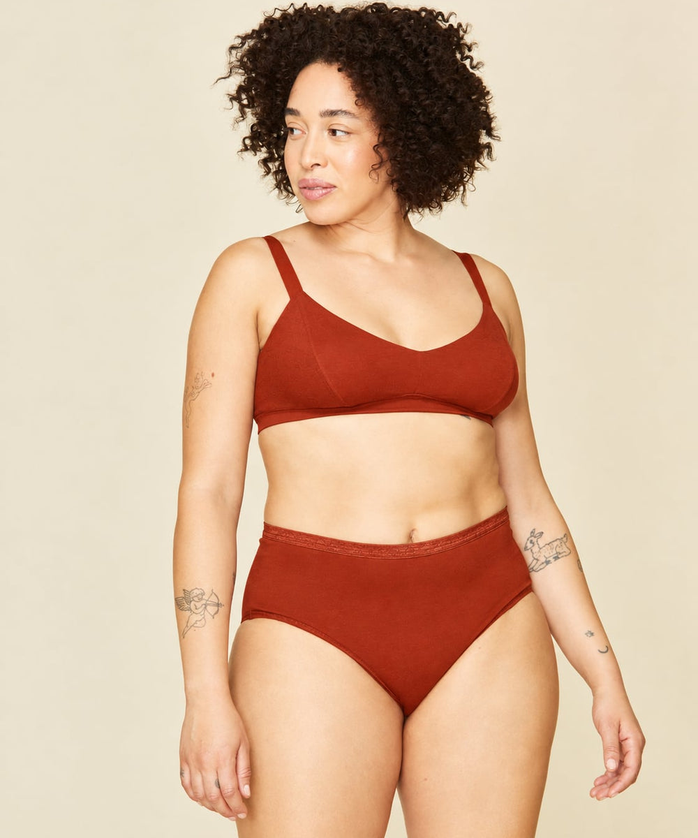 A woman modeling a terracotta-colored mid rise brief against a solid beige background.
