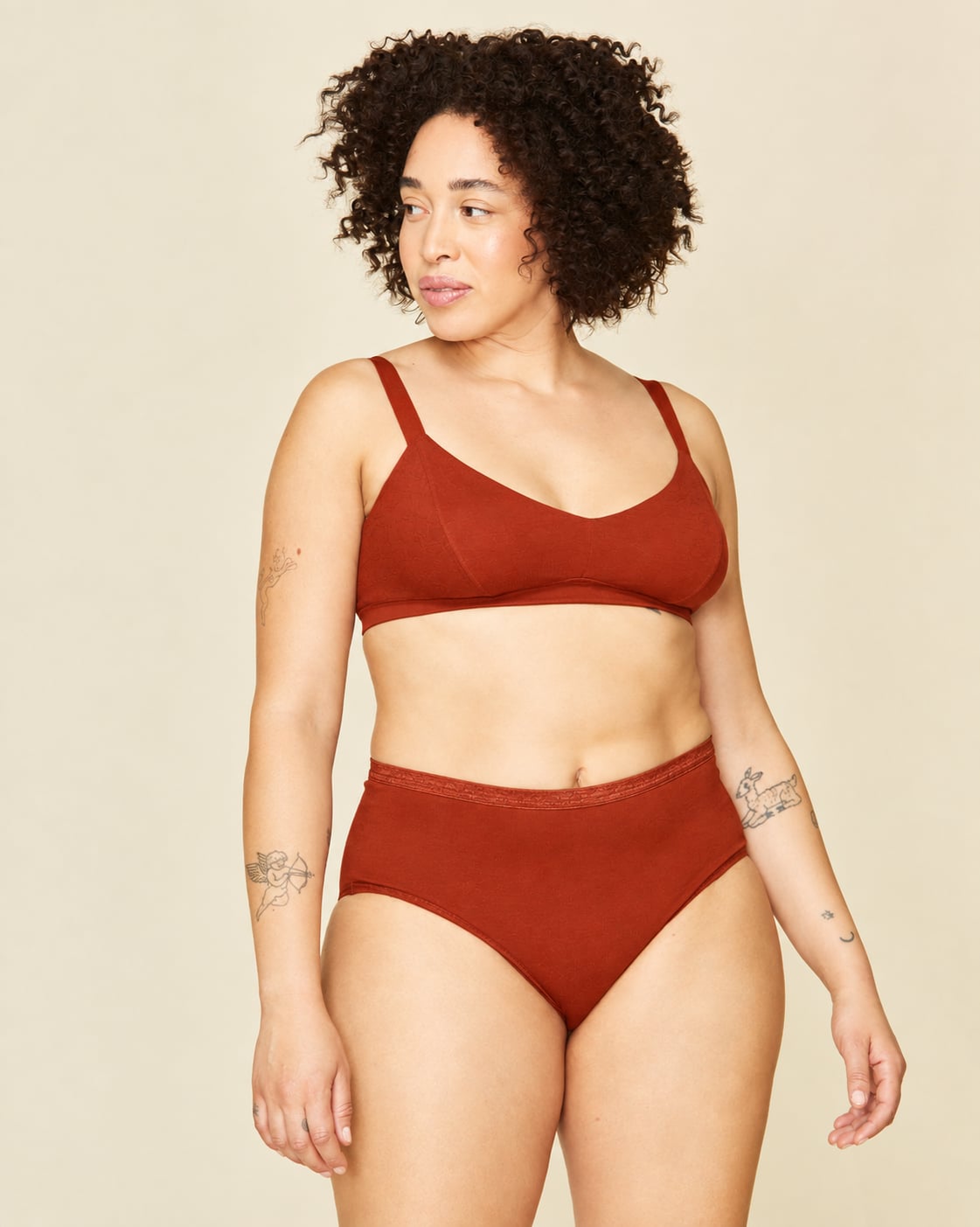 A woman modeling a terracotta-colored mid rise brief against a solid beige background.