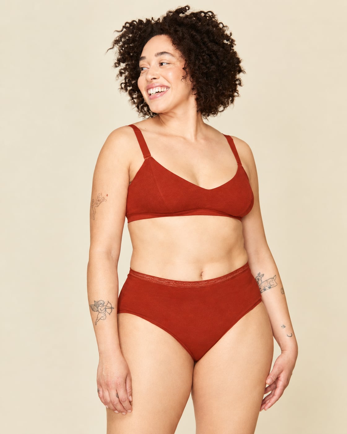 A woman modeling a mid rise brief in solid terracotta orange color, standing against a plain beige background.