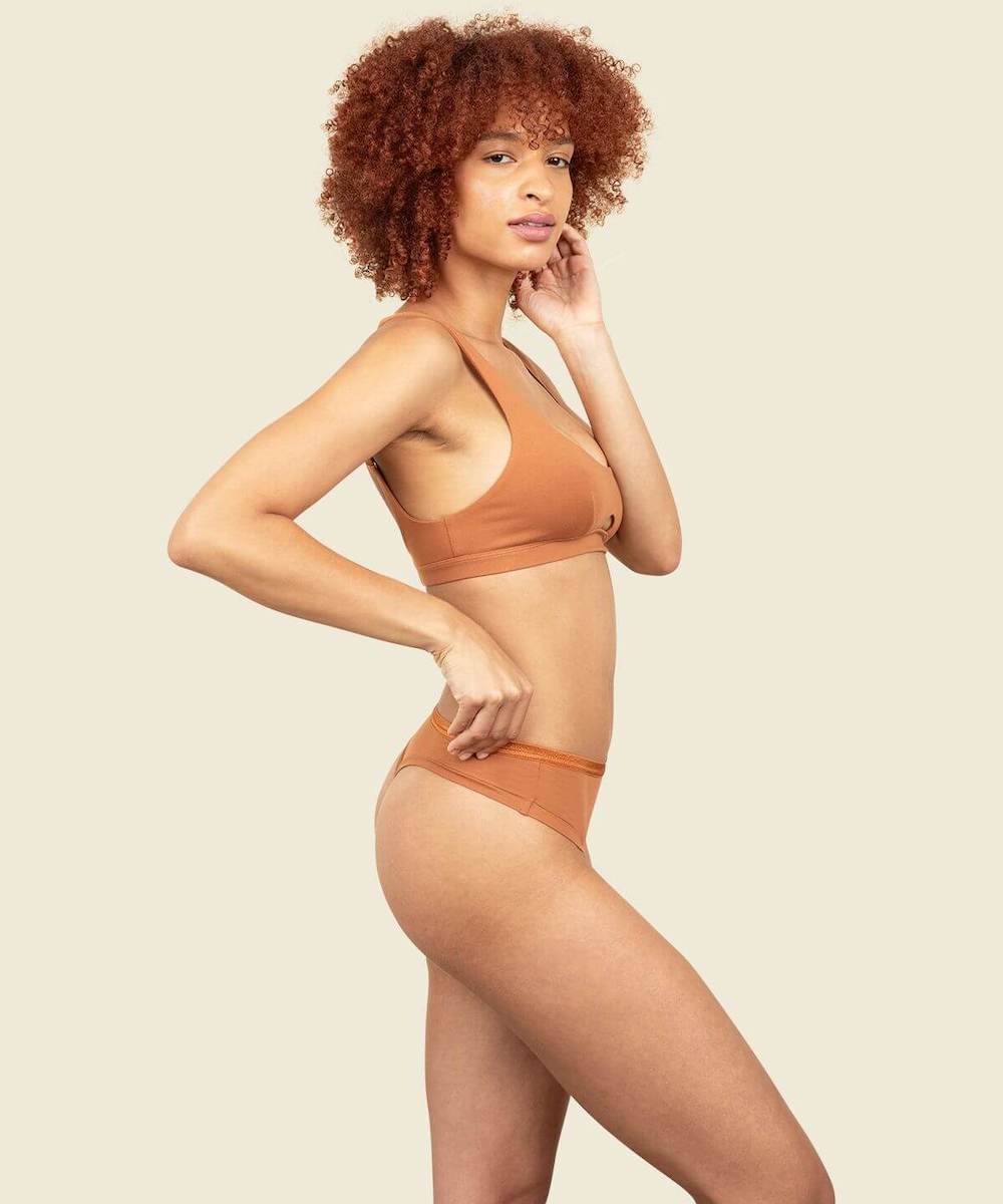 Woman in organic cotton mid-rise thong and keyhole soft bra in spice orange brown color.